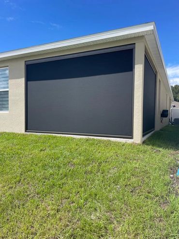Modern house with black retractable outdoor screens on beige walls and green lawn.