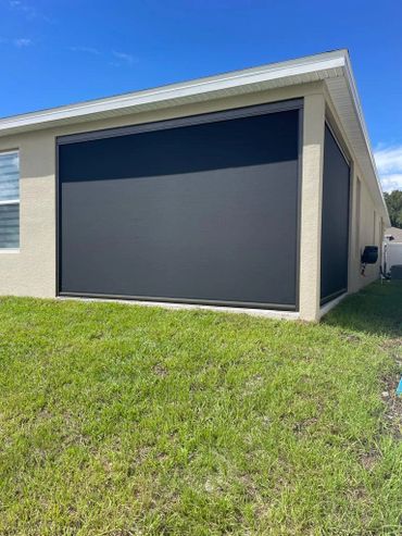 Modern house with black retractable outdoor screens on beige walls and green lawn.