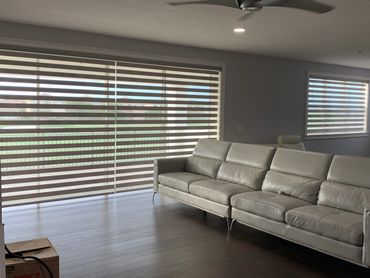 Modern living room with a gray leather sofa and large striped window blinds.
