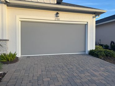 Modern gray garage door with house number 2781 and brick driveway.