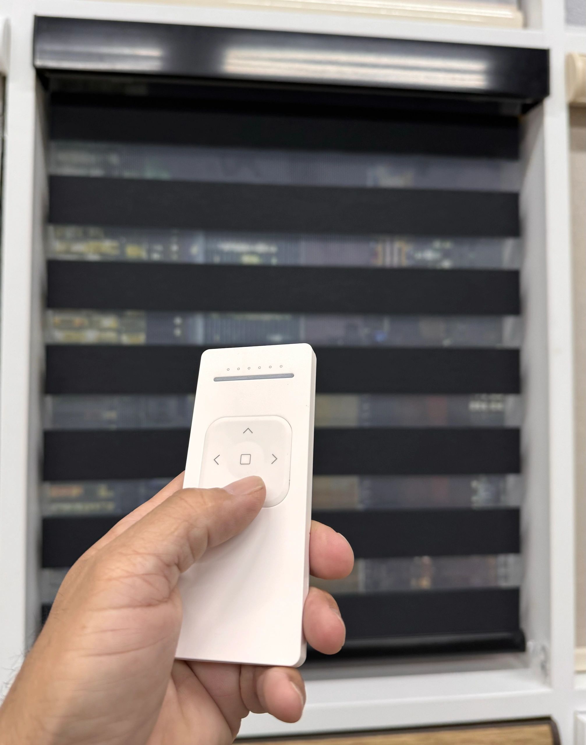Hand holding a white remote controlling black window blinds.