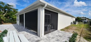 Modern white house with black window screens and a paved patio area under a blue sky.