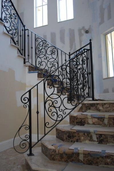 Elegant staircase with ornate black wrought iron railing and marble steps under construction.