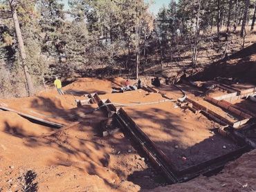 Construction workers preparing foundation forms in a wooded area.