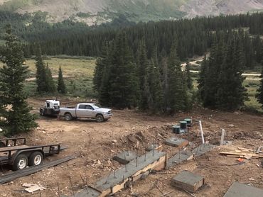 Construction site with concrete foundation in a mountainous forested area.