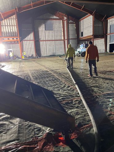 Workers preparing a large indoor construction site with metal framework and concrete pouring.
