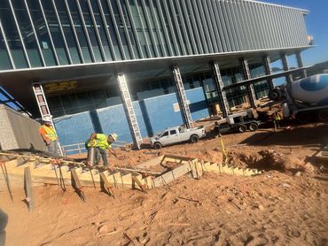 Construction workers preparing wooden forms at a building site under a modern glass structure.