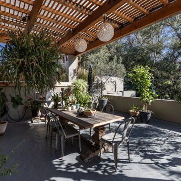 Cozy outdoor dining area with wooden table and hanging plants under a pergola.