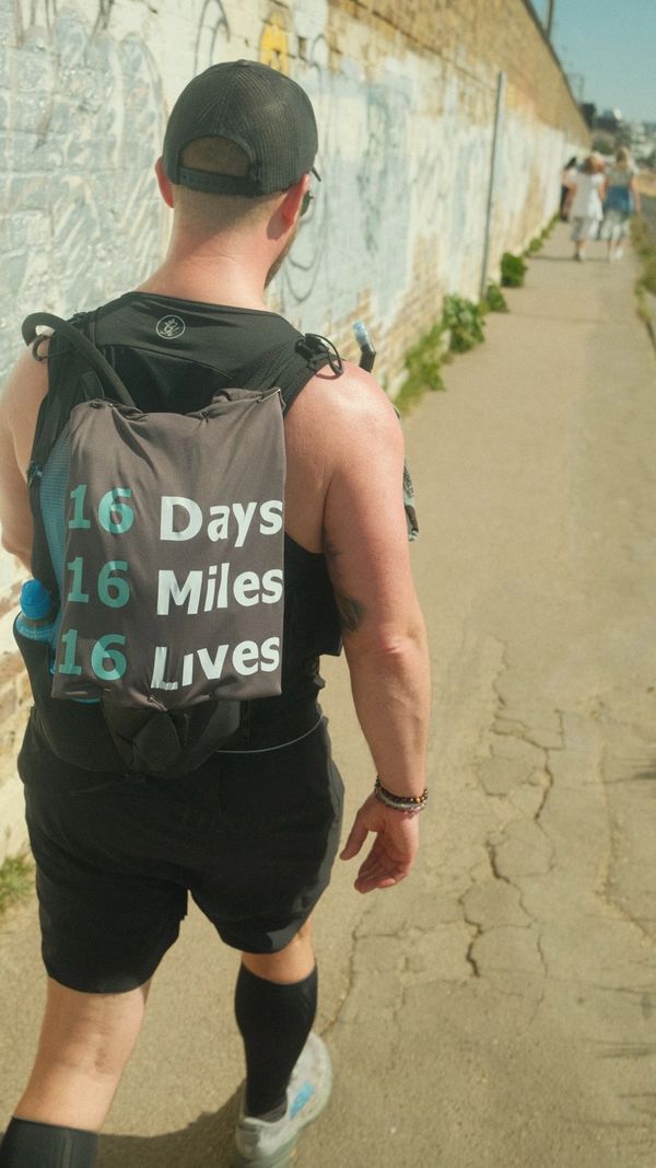 Man walking with a backpack that reads '16 Days 16 Miles 16 Lives'.
