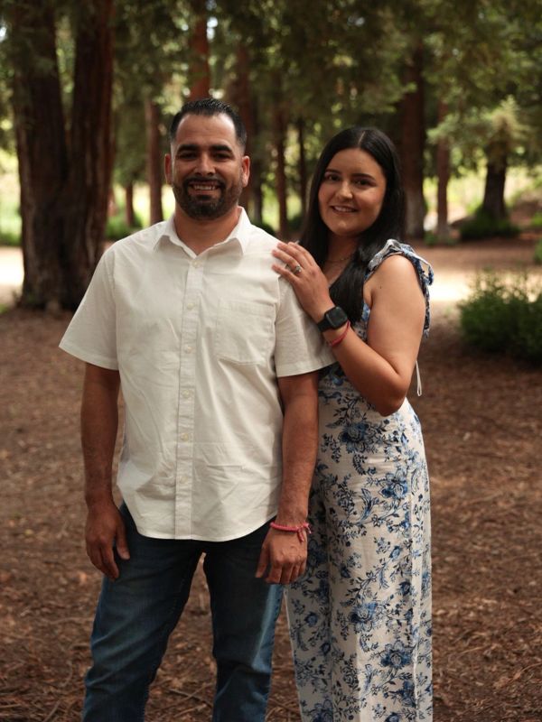Couple smiling outdoors in a forested area.