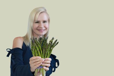 Woman smiling and holding fresh asparagus in front of a plain background.