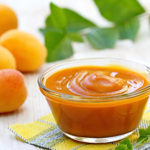 A bowl of smooth apricot puree with fresh apricots in the background.