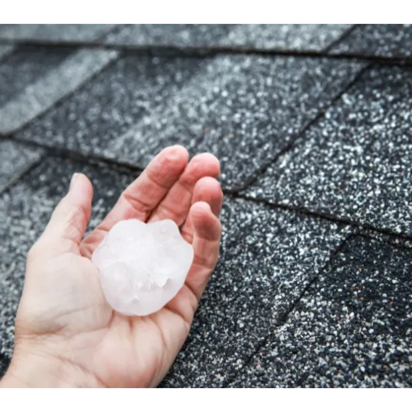 A hand holding a large hailstone on a rooftop.