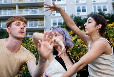 Three dancers reach across one another over lapping hands and arms gazing in different directions.