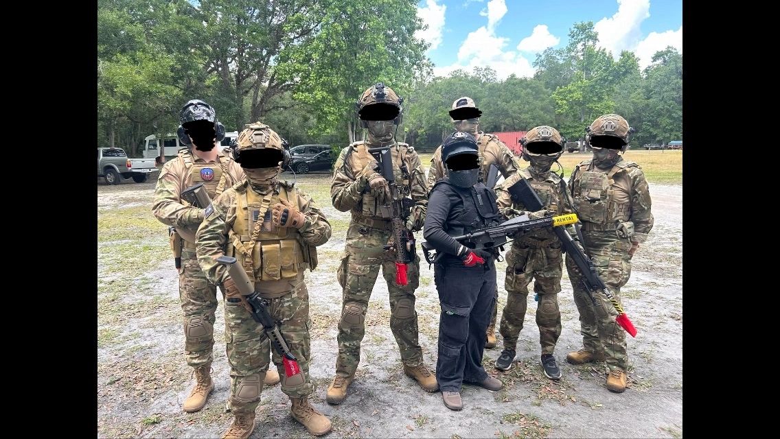 Group of seven people in tactical gear posing outdoors.