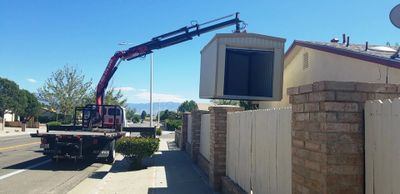 Boom truck delivering portable storage shed over fence. Backyard storage, back yard storage, storage