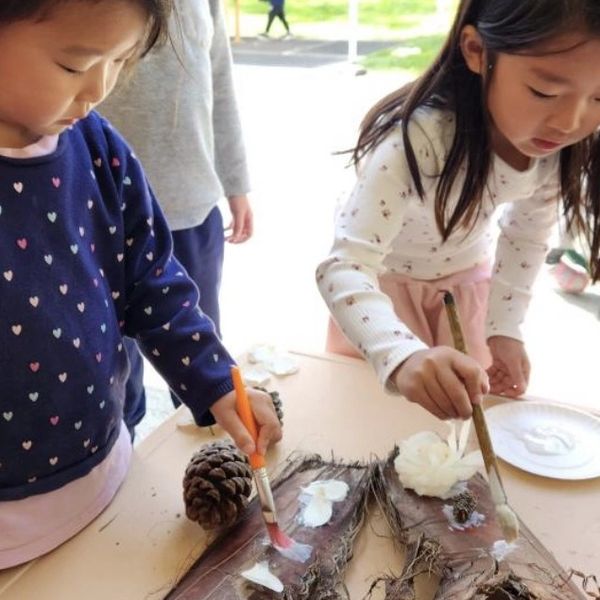 Two young girls painting on large dried leaves at a table outdoors.