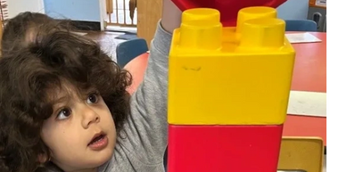 Child playing with a tall stack of colorful building blocks indoors.