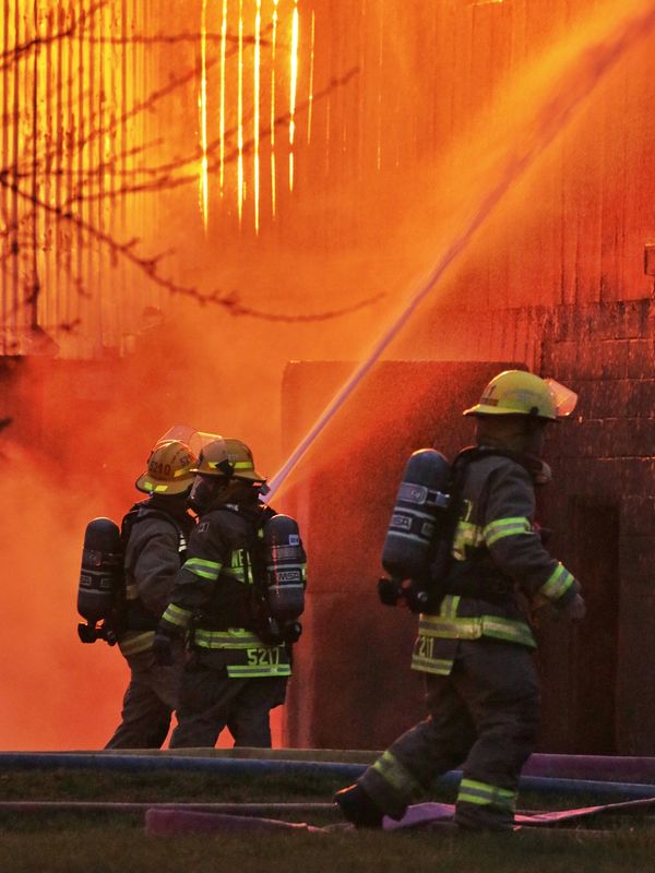 Firefighters battle a blazing fire with water hoses amidst heavy smoke.