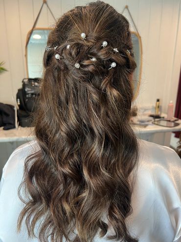 Elegant half-up braided hairstyle adorned with pearl pins on wavy brown hair.
