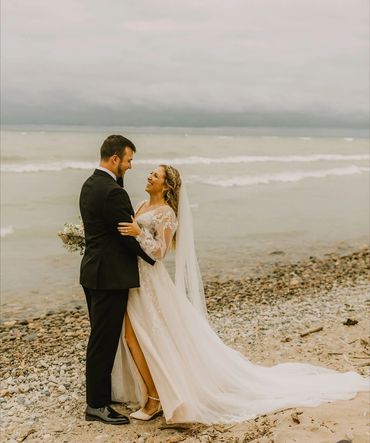 Bride and groom embracing on a rocky beach, sharing a joyful moment.