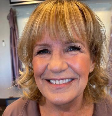 Close-up of a smiling mature woman with blonde hair and bright eyes.