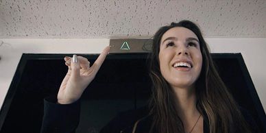 Image of a teenage girl pointing up in front of an elevator.
