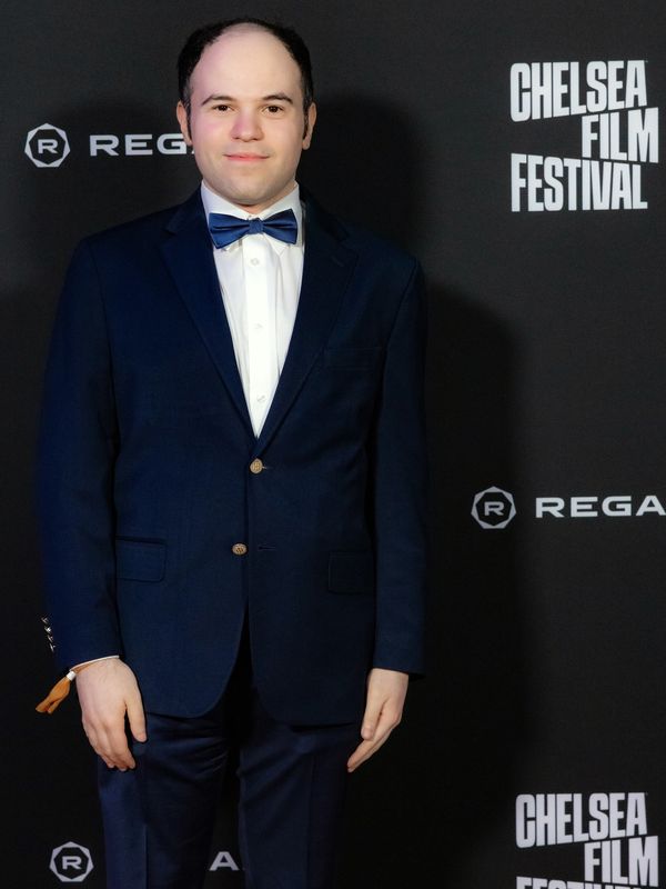 A man in a suit and bowtie in front of step-and-repeat.