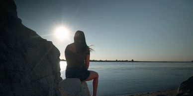Image of girl on a rock on the beach, looking at the sun.