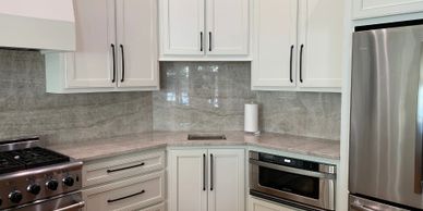 A kitchen with white cabinets and beige quartzite countertops with full height backsplash