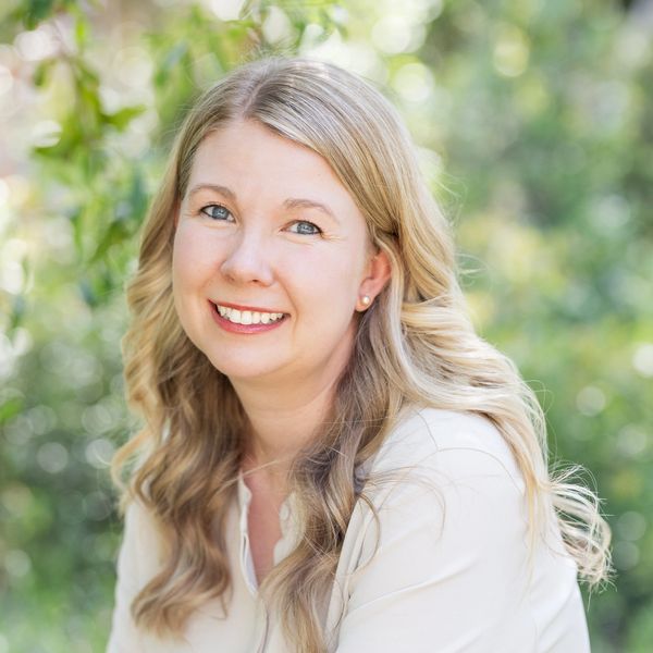 Smiling woman with long blonde hair outdoors in soft natural light.