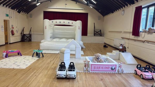 Indoor play area with toys and a white bouncy castle in a hall.