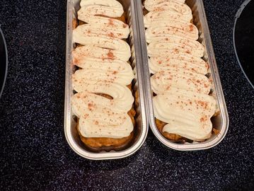Two pumpkin bread loaves with cream cheese frosting sprinkled with cinnamon.