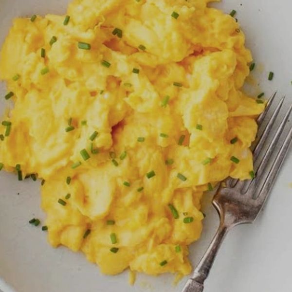 Scrambled eggs garnished with chives on a plate with a fork.