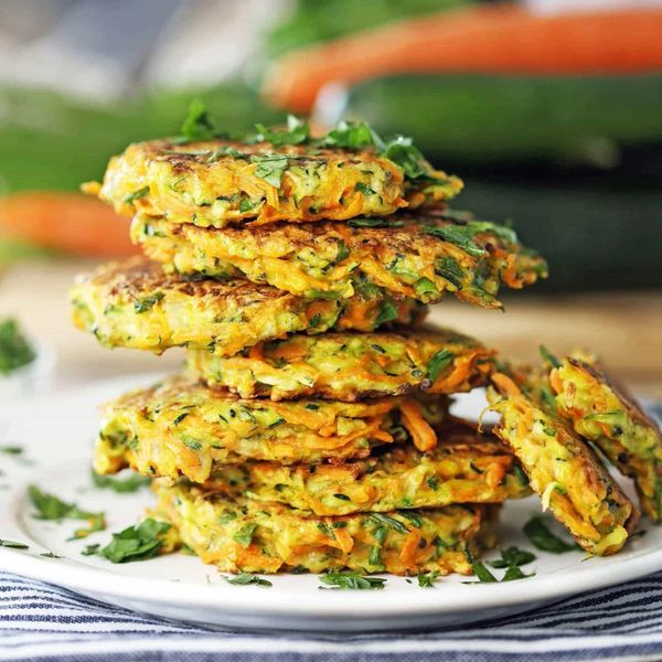 Stack of golden vegetable fritters garnished with fresh herbs on a plate.
