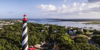 Striped lighthouse overlooking coastal town and water.