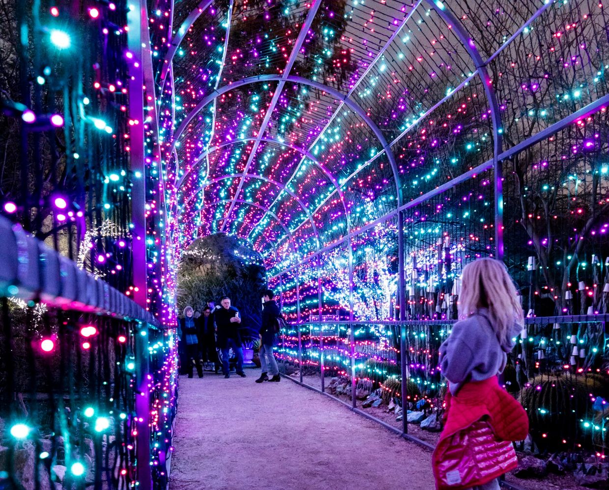 People walk through a colorful tunnel of blue, pink, and purple lights.