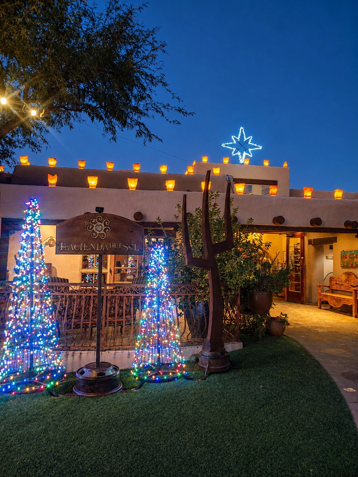 Hacienda del Sol decorated with colorful Christmas lights and glowing luminarias at dusk.