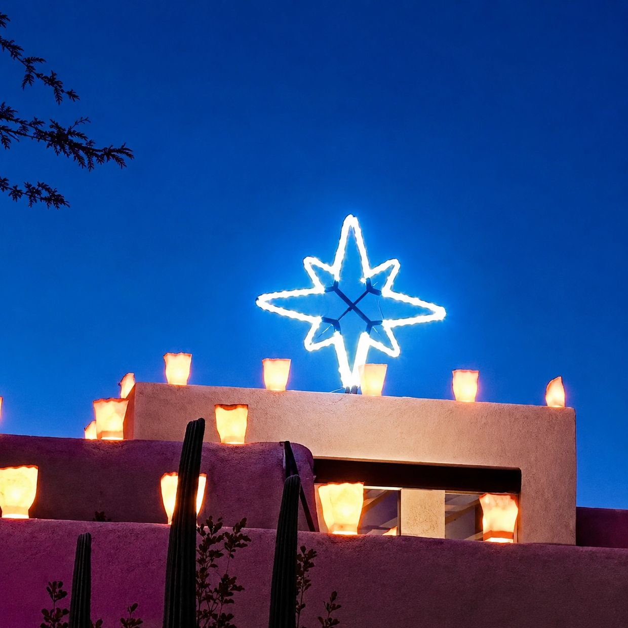 Light luminarias and a glowing star adorn an adobe rooftop at twilight.