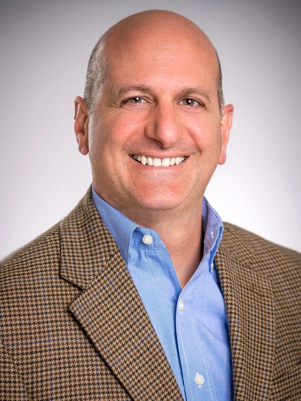 Smiling bald man in a brown houndstooth blazer and blue shirt.