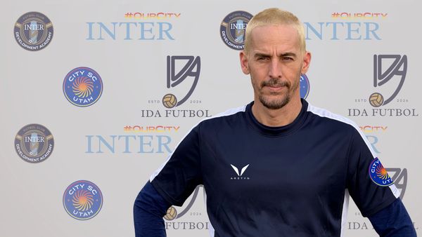 Man with blonde hair in sportswear posing in front of soccer-related backdrop.