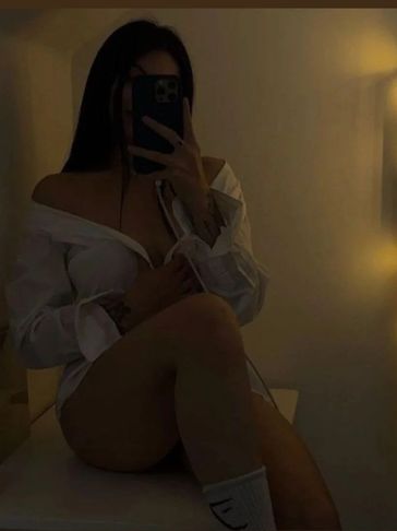 Person taking a dimly lit mirror selfie wearing a white shirt and socks.