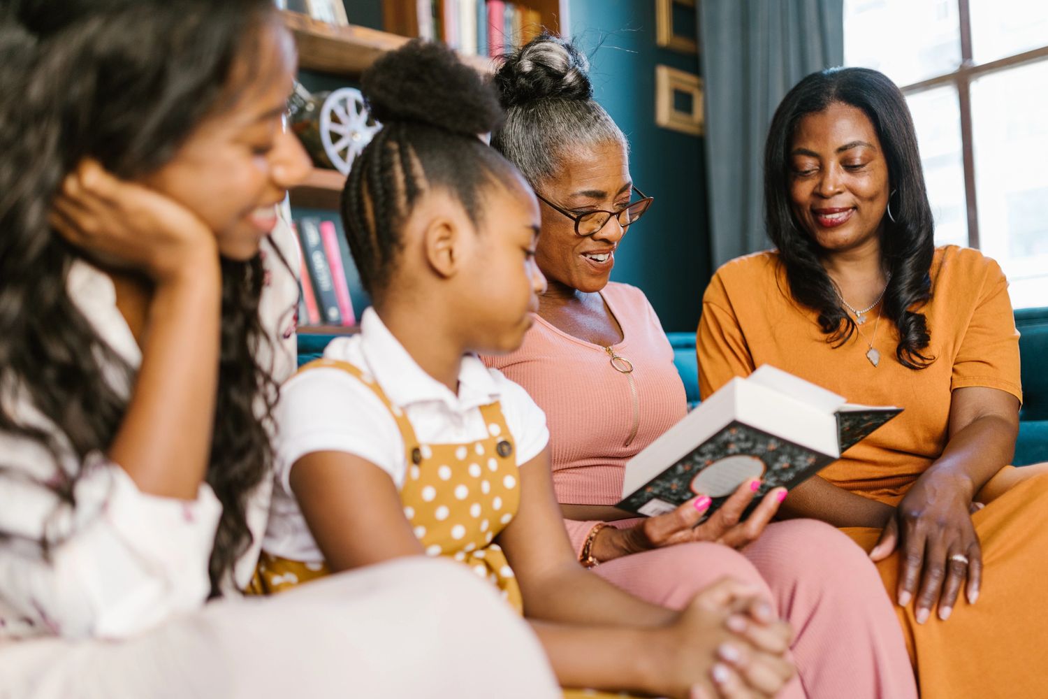 Two adult women reading to two younger girls, all are smiling and happy.