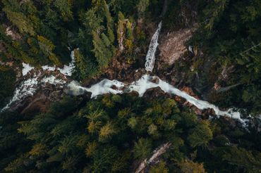 Aerial view of a river flowing through a dense forest with rocky edges.