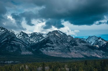 Snow-capped mountains over a dense forest under a cloudy sky.