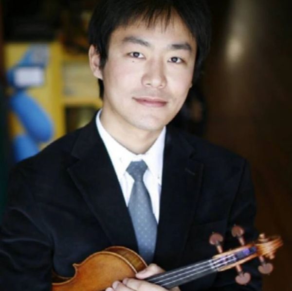 Shaoqing Xu in a black suit, holding a violin, and posing for a photo