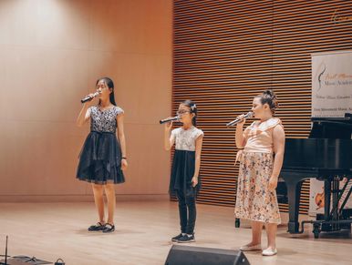 The image shows three young individuals, likely children or pre-teens, on a stage performing