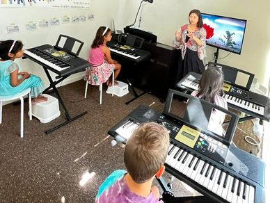 group piano lesson in progress, with an instructor teaching several children