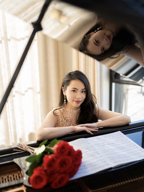 Dr. Christina Chen posing with a piano, sheet music, and a bouquet of roses on top