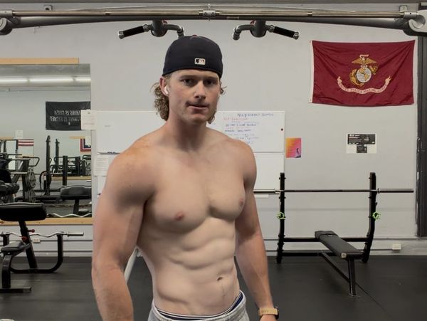 Muscular young man in a gym wearing a backwards cap and AirPods.